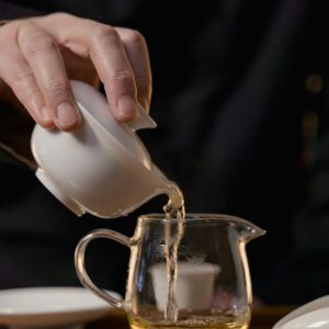 Pouring green tea from gaiwan to cha hai during a traditional tea ceremony.